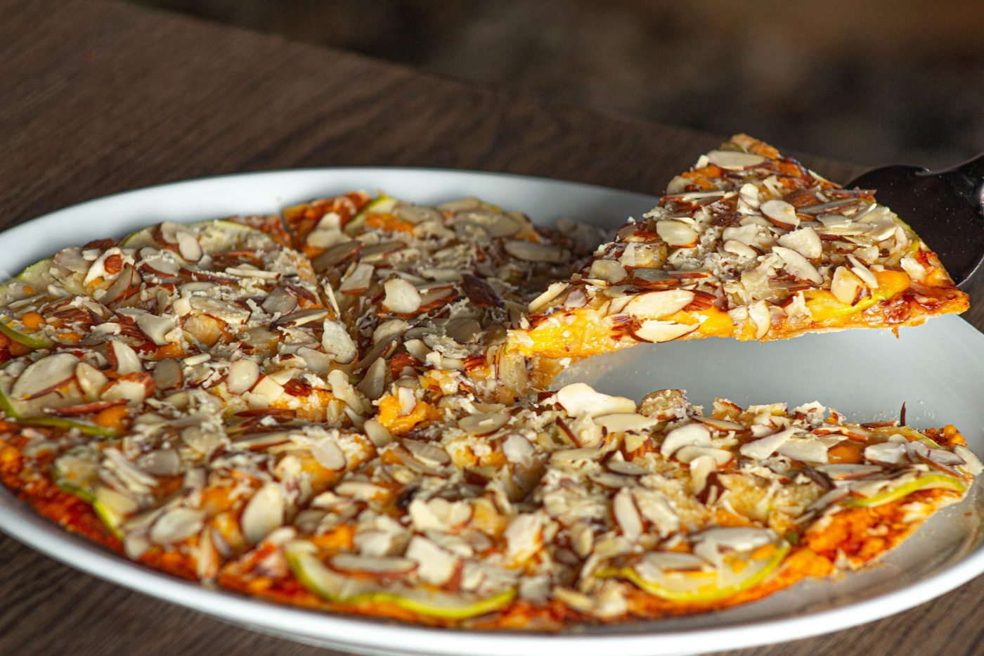 Porción de pizza 4 quesos con manzana levantada con la espátula: se ve la base delgada y crocante